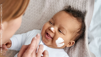 Eine Frau cremt das Gesicht eines Babys ein. 